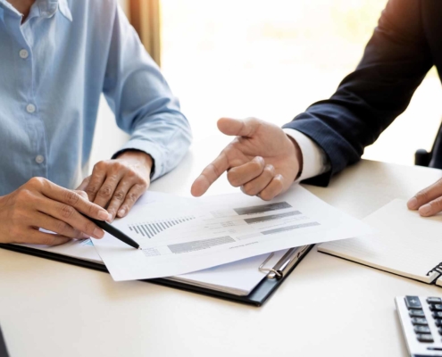 Two people in business casual attire pointing at a piece of paper